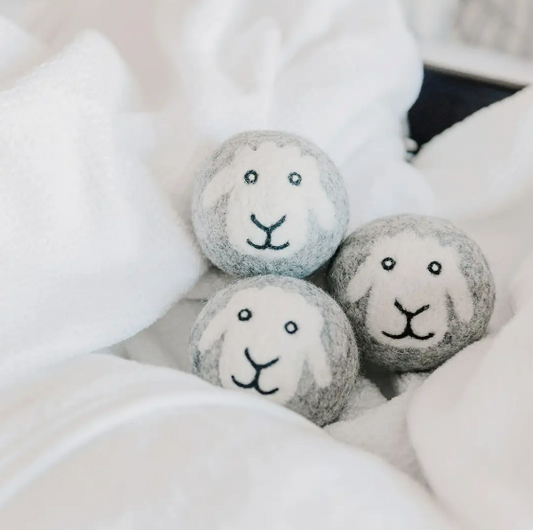 Three felted wool dryer balls with cute sheep faces nestled in a soft, white blanket.