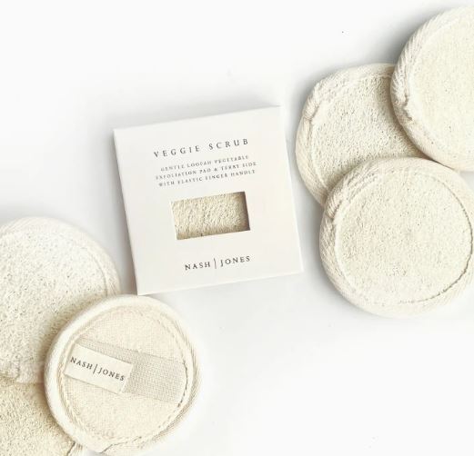 A collection of natural loofah vegetable sponge pads displayed next to their packaging labeled "veggie scrub" by nash | jones.