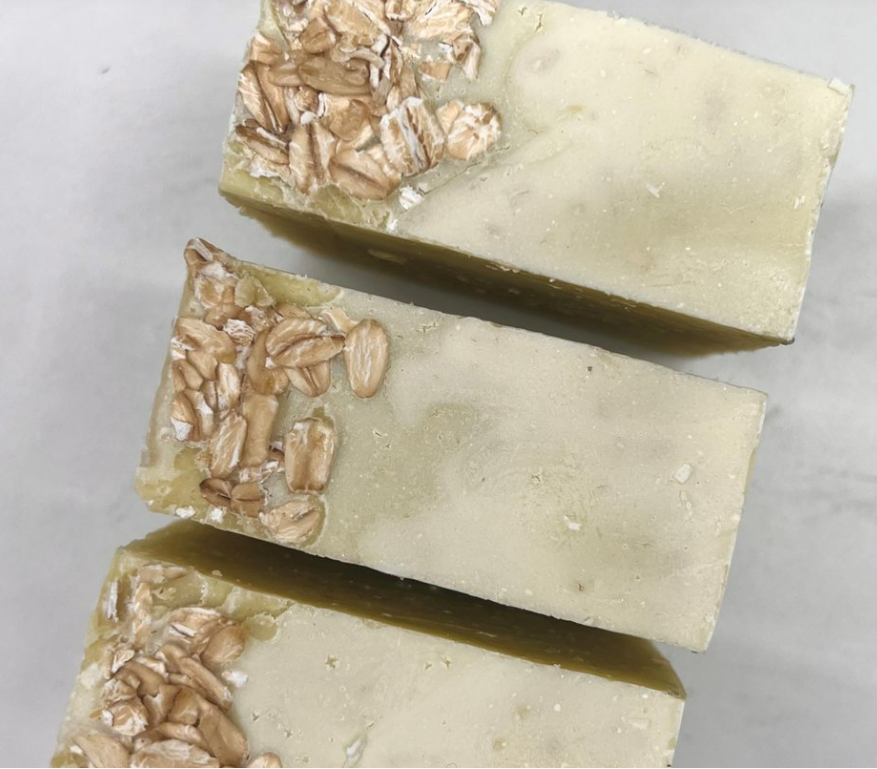 Handmade natural soap bars sprinkled with oats on top, laid out diagonally on a neutral background.