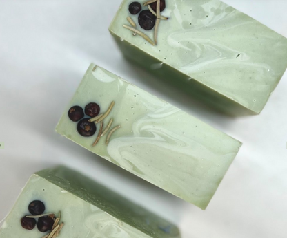 Three elegant, green-hued artisanal soap bars decorated with small botanical accents on a white background.