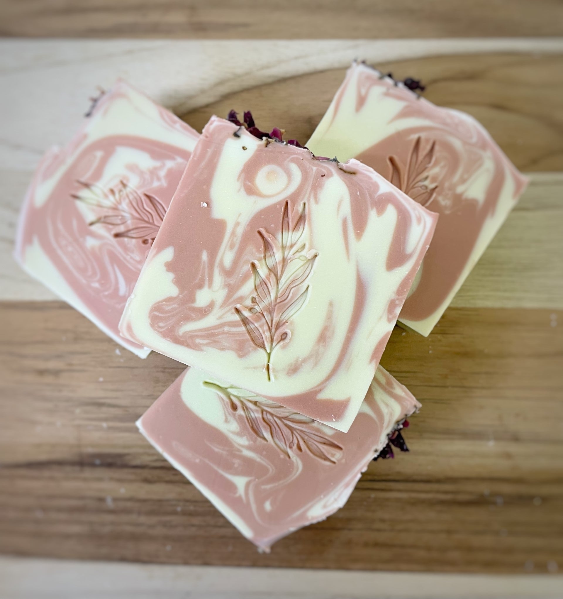 Handcrafted artisanal soap bars with a pink and cream swirl design, embellished with botanical elements on a wooden surface.