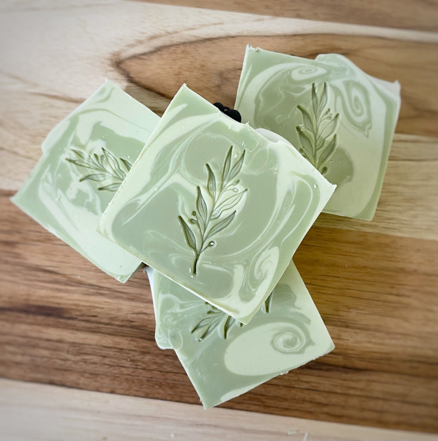 Artisanal green swirl soaps with delicate leaf imprints, arranged beautifully on a wooden surface.