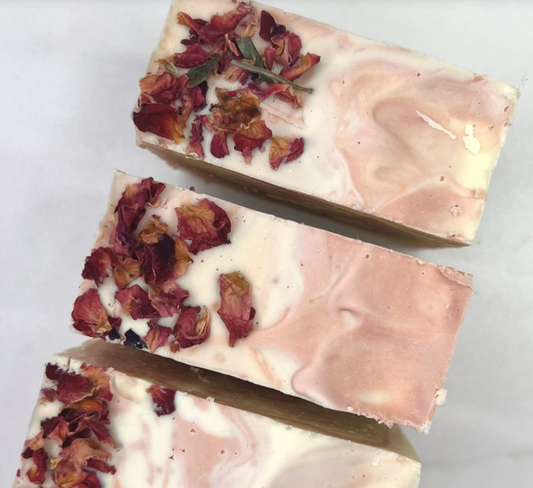 Three bars of handmade soap adorned with dried rose petals on a white background.